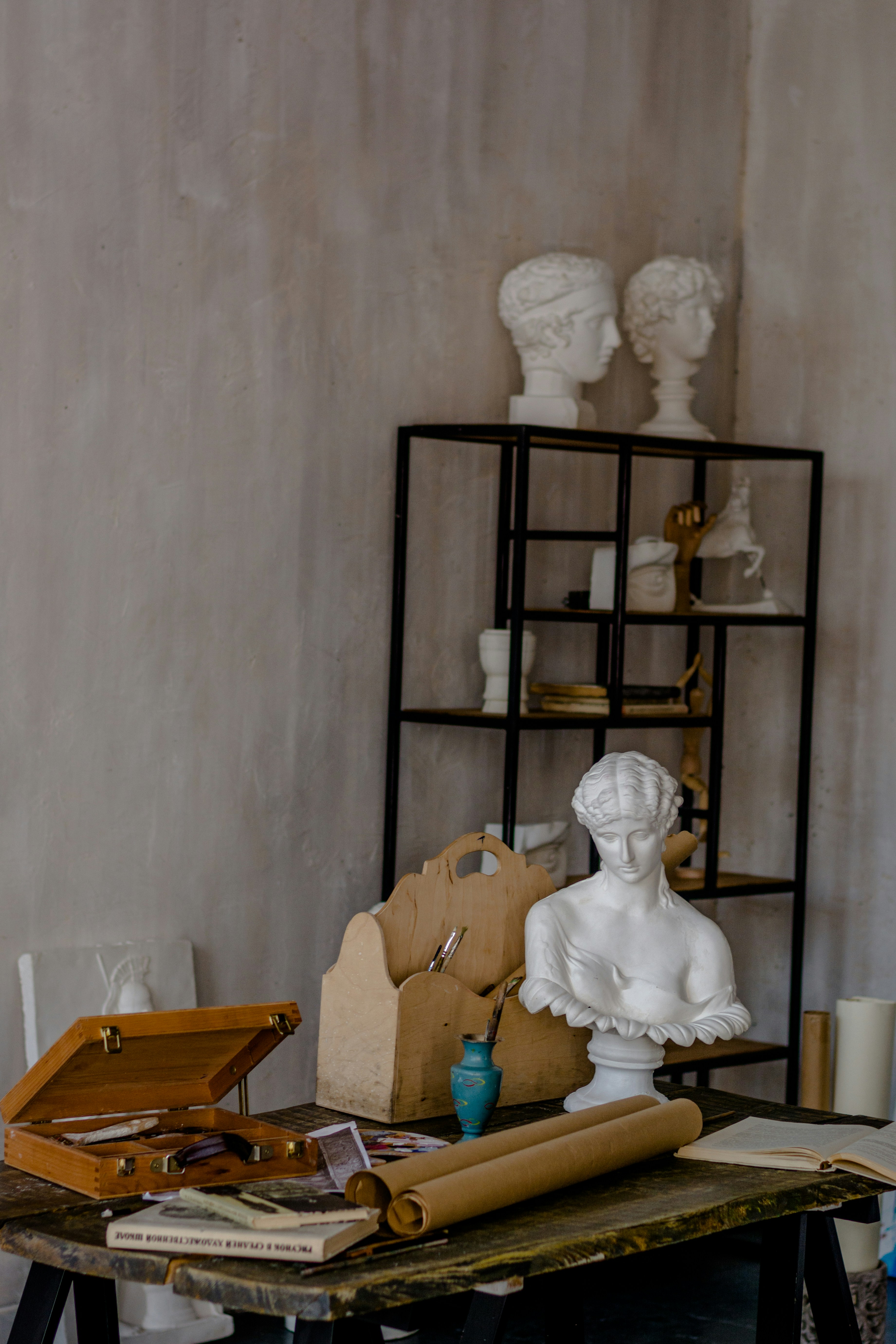 Atelier studio scene with classical marble busts on a shelf, an artist's worktable with scrolls, paintboxes, and art supplies